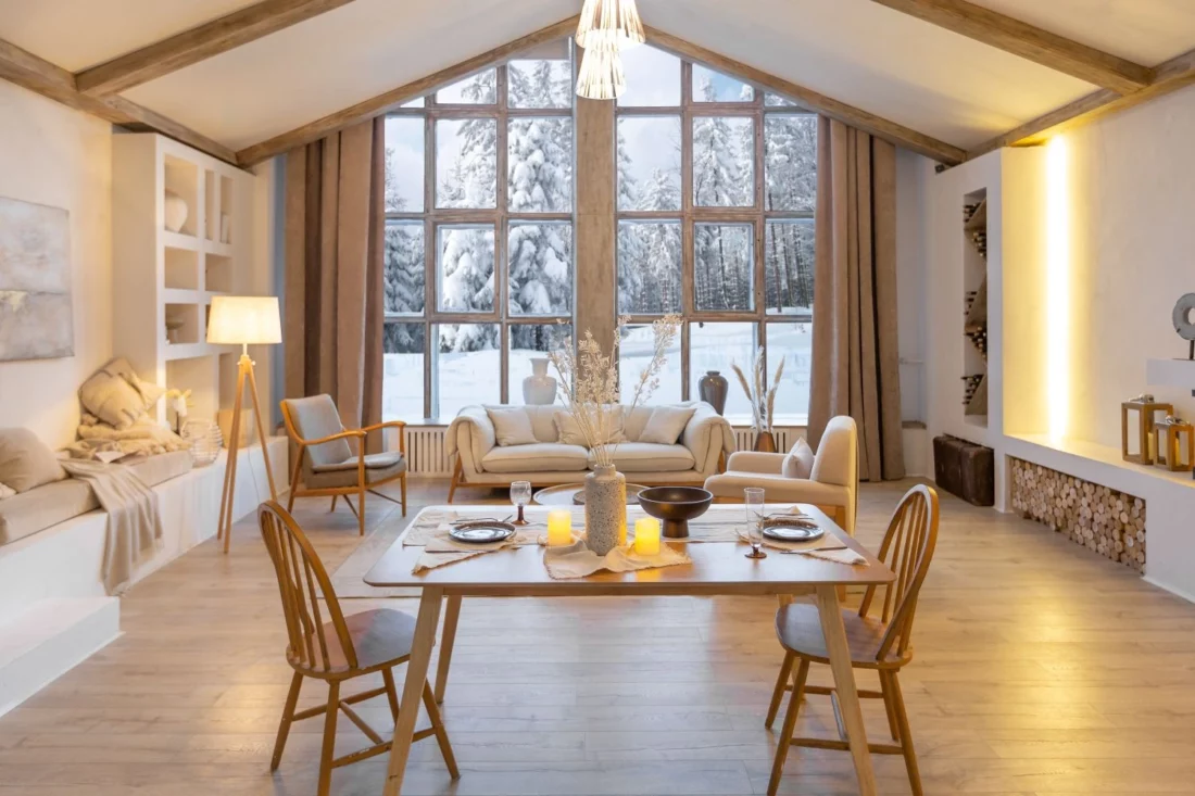 Arredamento per casa vacanze in montagna: soggiorno in stile scandinavo con mobili in legno, luci calde e vista panoramica sulla neve