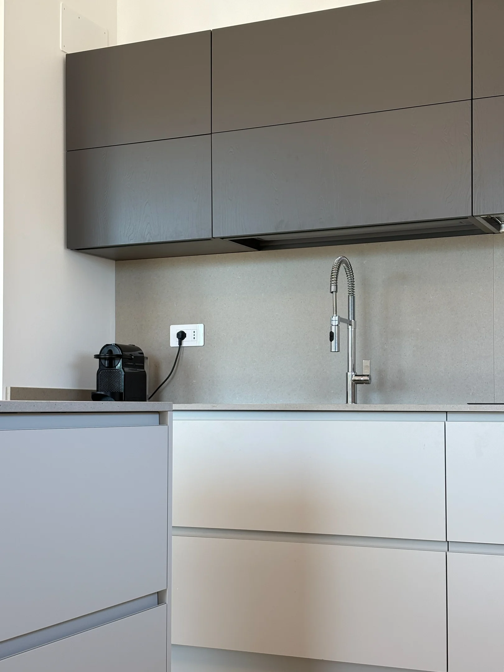 Dettaglio di una cucina moderna su misura, con pensili grigio antracite, basi bianche, piano effetto pietra e rubinetto professionale in acciaio.