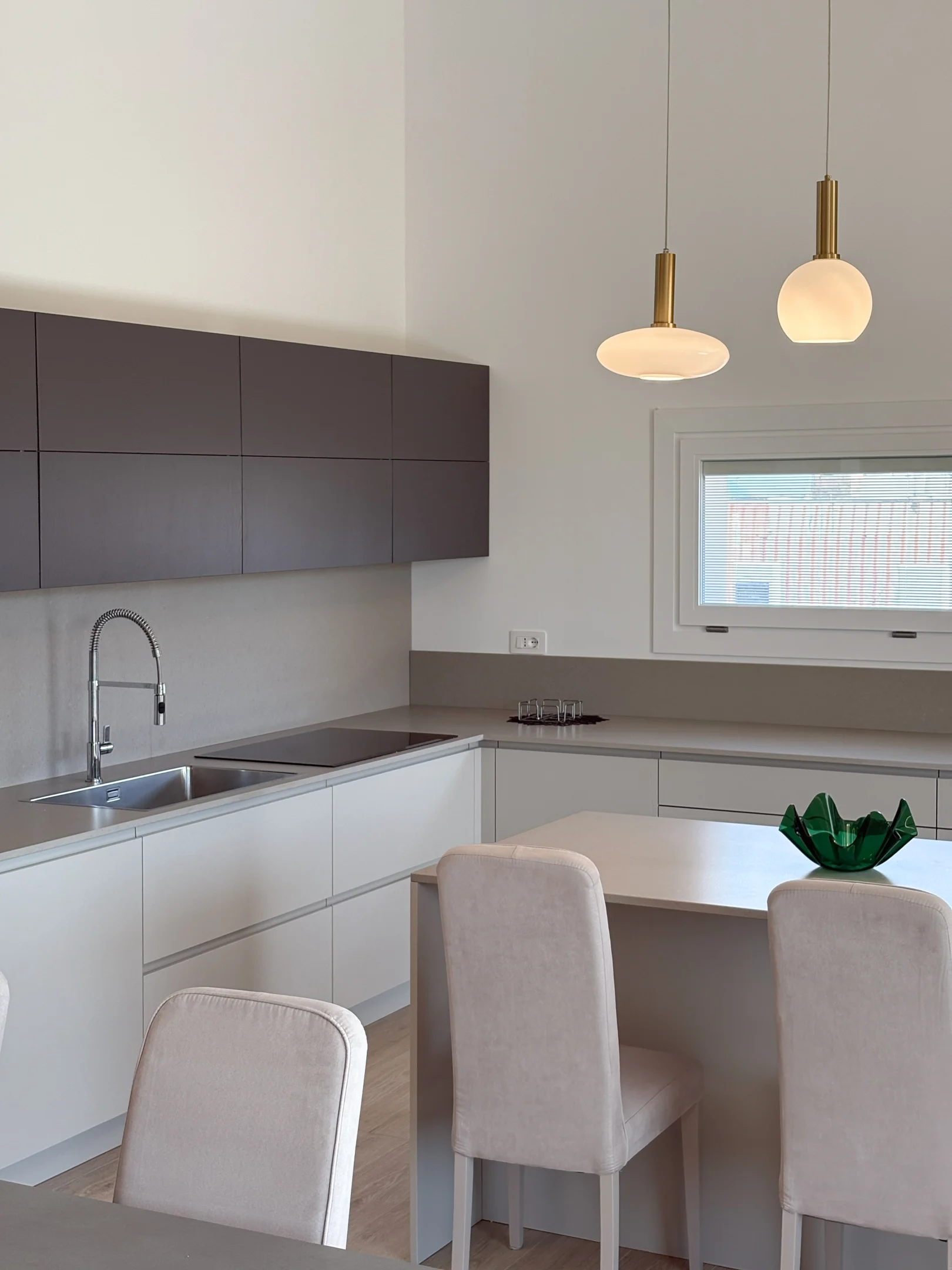 Cucina moderna su misura con finiture bianche e grigio antracite, penisola centrale, piano effetto pietra e lampade a sospensione dal design elegante.